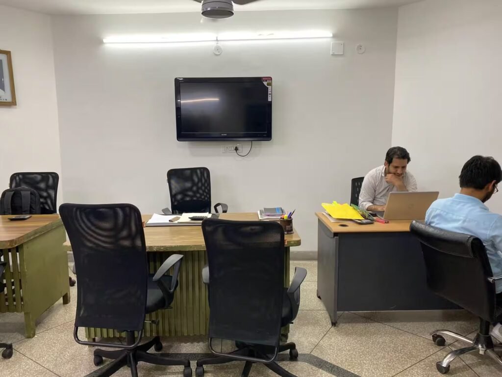 Interior view of the Ashvin & Company corporate office space featuring employee workstations with laptops, mesh office chairs, wooden desks, and a wall-mounted Sony Bravia television display.