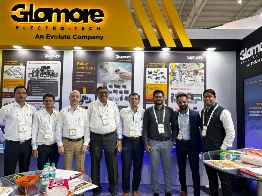 A team of seven representatives standing together in front of the illuminated Glomore Electro-Tech company exhibition booth showcasing product displays.