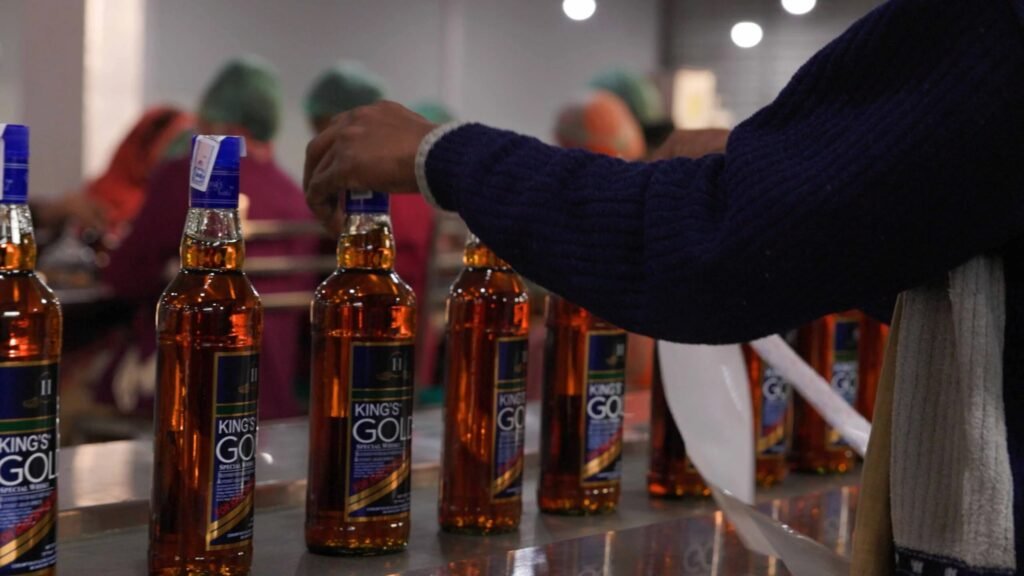 Close-up of glass bottles of King's Gold Special Whisky moving along a conveyor belt, with factory workers handling them on the production line.